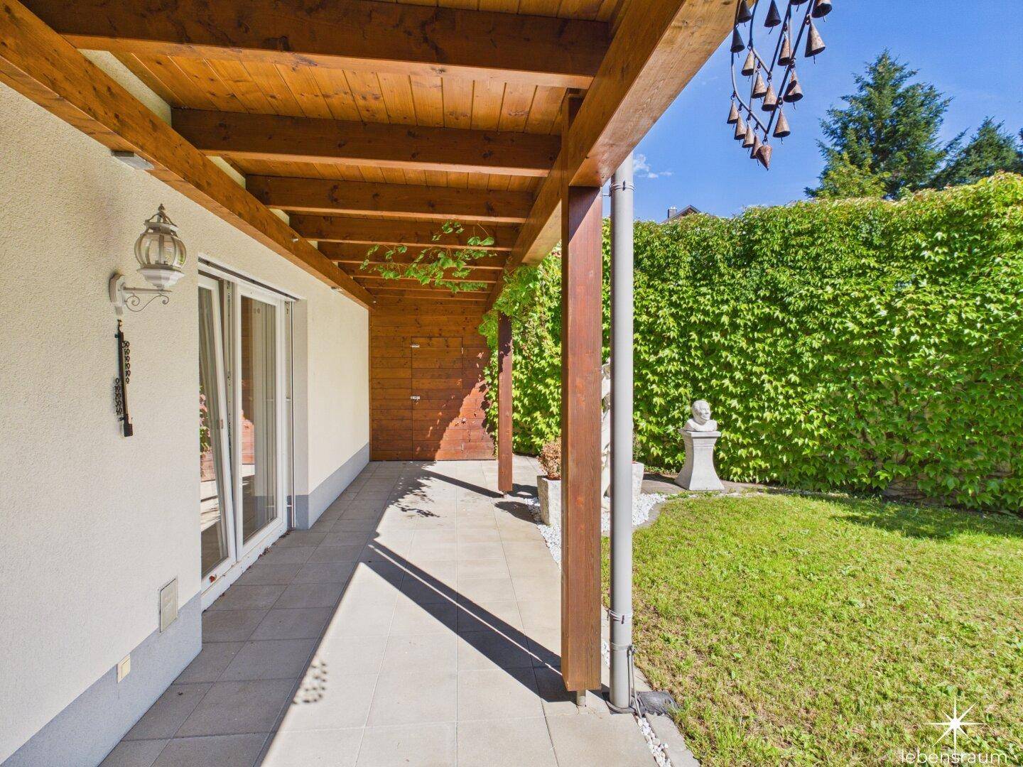 Überdachte Terrasse mit Holzdach und Blick auf den grünen, gepflegten Garten.