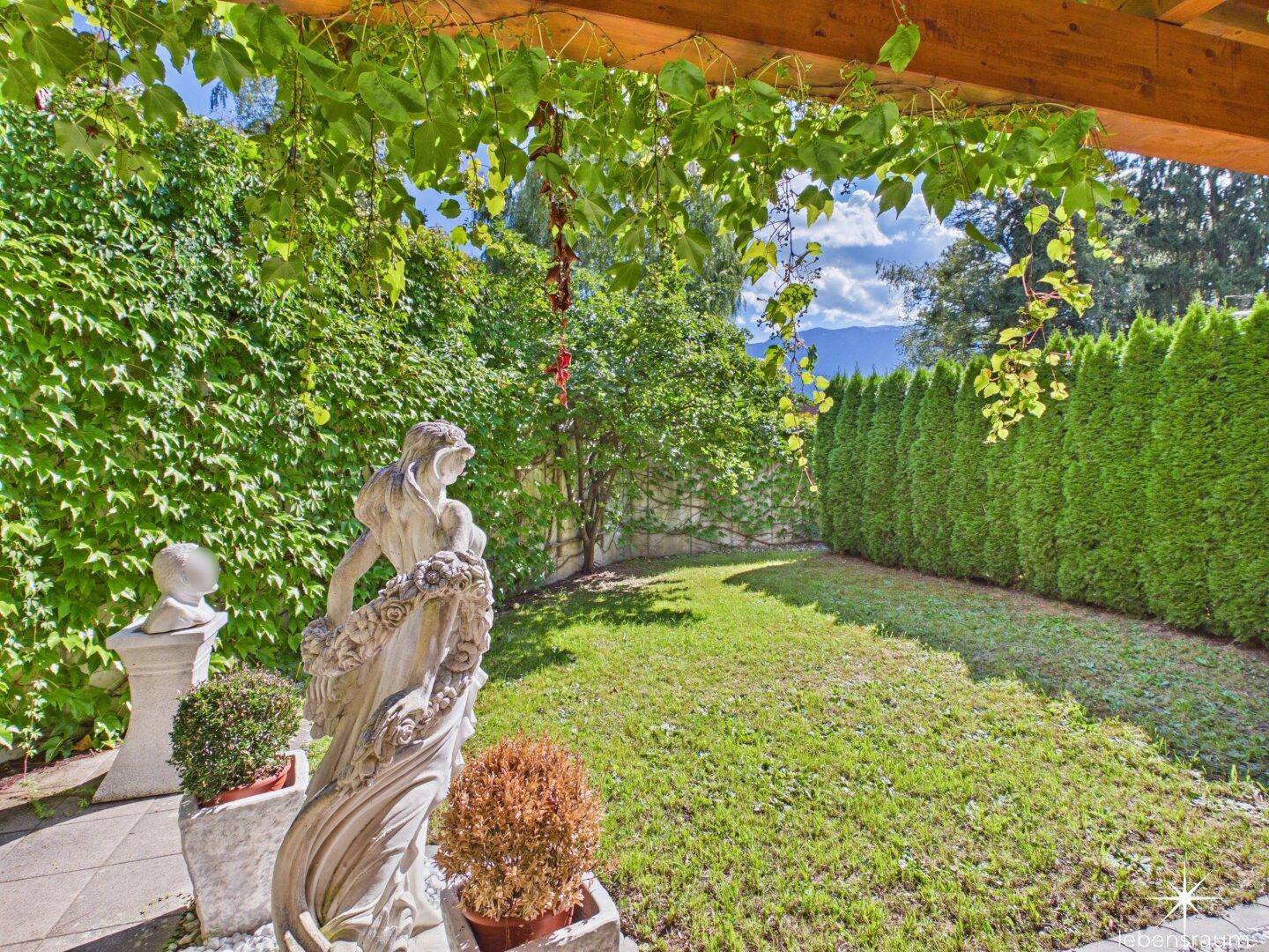 Gepflegter Gartenbereich mit grüner Hecke und malerischem Bergblick im Hintergrund.