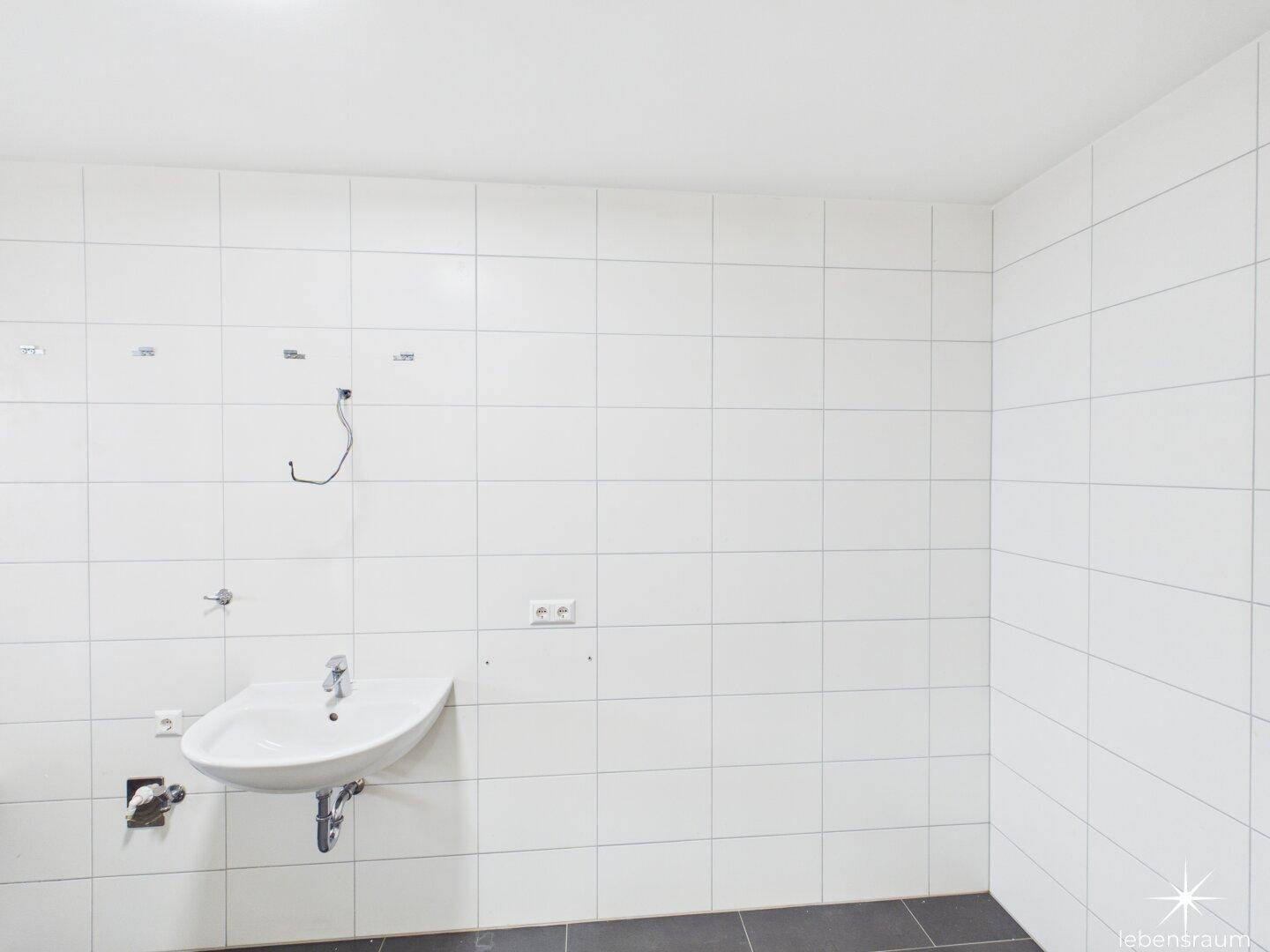 Unfertiges Badezimmer mit weißen Wandfliesen und einem Waschbecken.