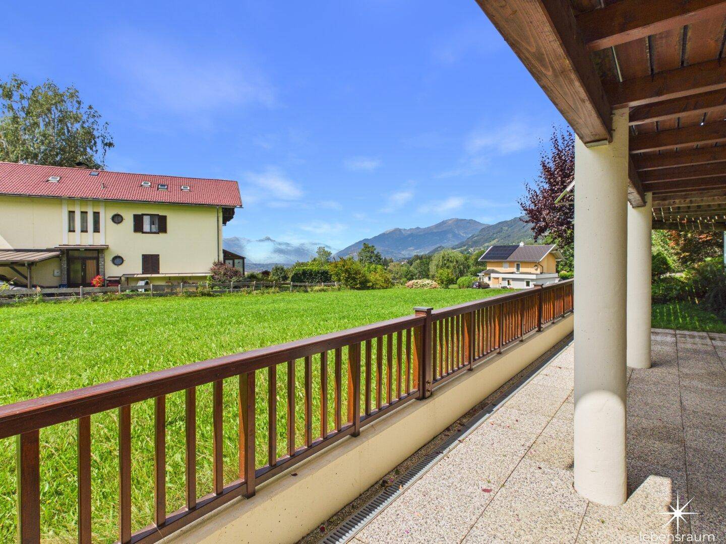 Überdachte Terrasse mit weitem Blick über grüne Wiesen und die umliegende Landschaft.