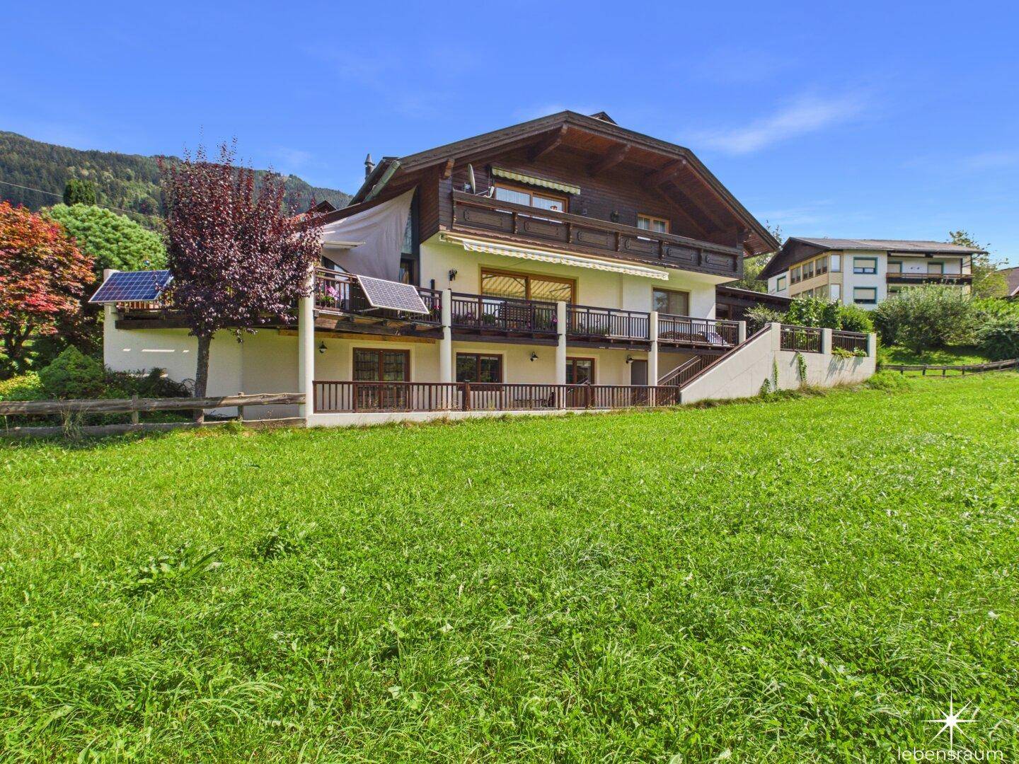 Ansicht des Hauses mit mehreren Balkonen und einer weiten Rasenfläche im Vordergrund.