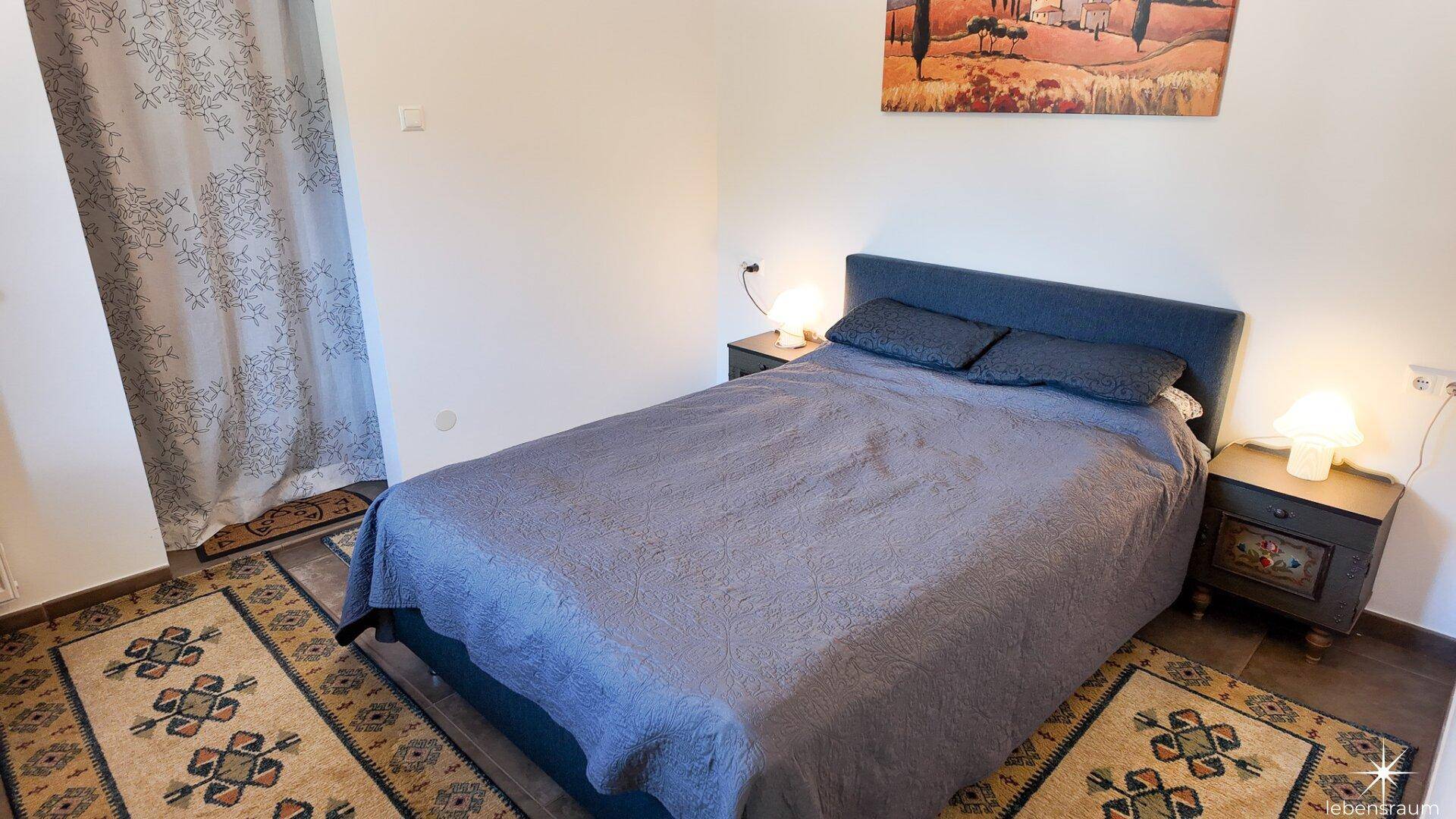 Gemütliches Schlafzimmer mit Doppelbett, Nachttischen und dekorativen Teppichen.
