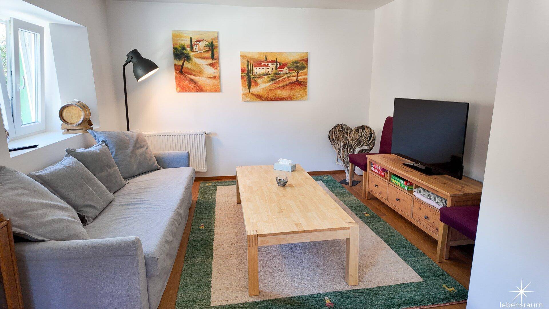 Helles Wohnzimmer mit bequemem Sofa, Holztisch und Fernseher, dekoriert mit Wandbildern.
