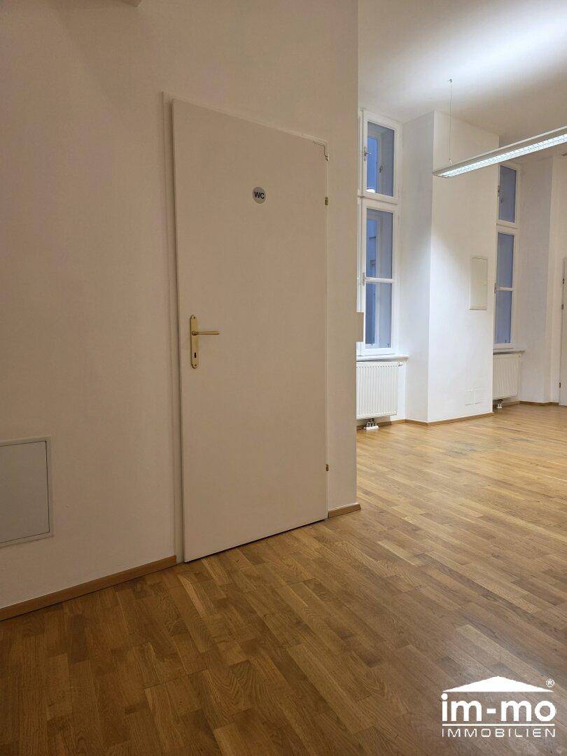 Heller Flur mit Holzboden und einer Tür, die zu einem WC führt, mit Blick auf Fenster.