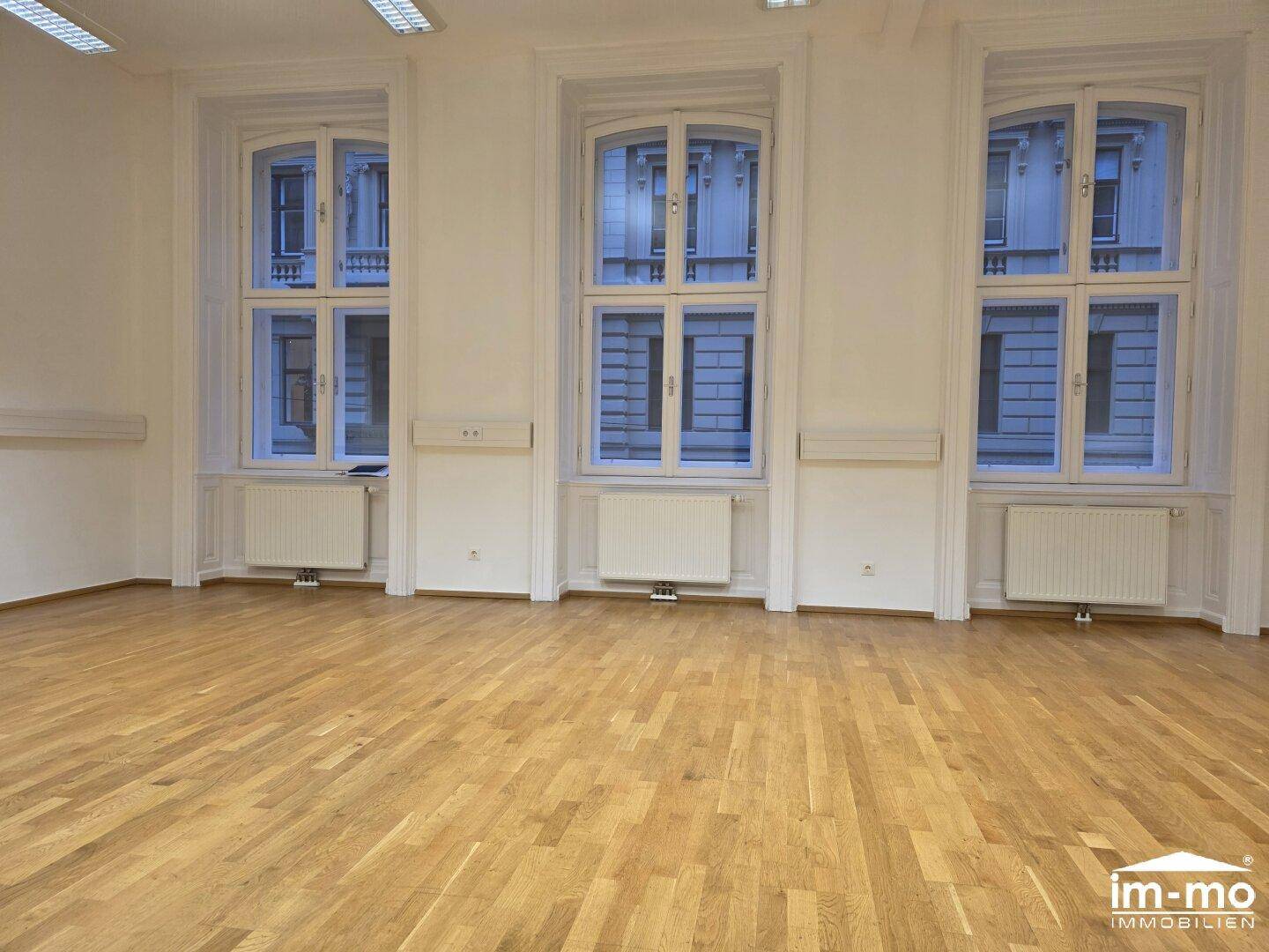 Geräumiger, heller Raum mit Holzboden und drei großen Fenstern, geeignet für verschiedene Nutzungen.