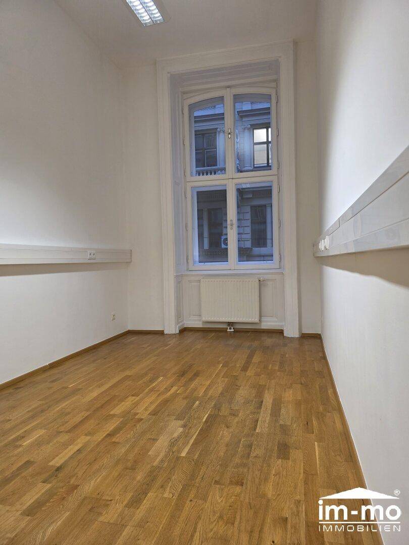 Einzelner Raum mit Holzboden und einem großen Fenster, das viel natürliches Licht hereinlässt.