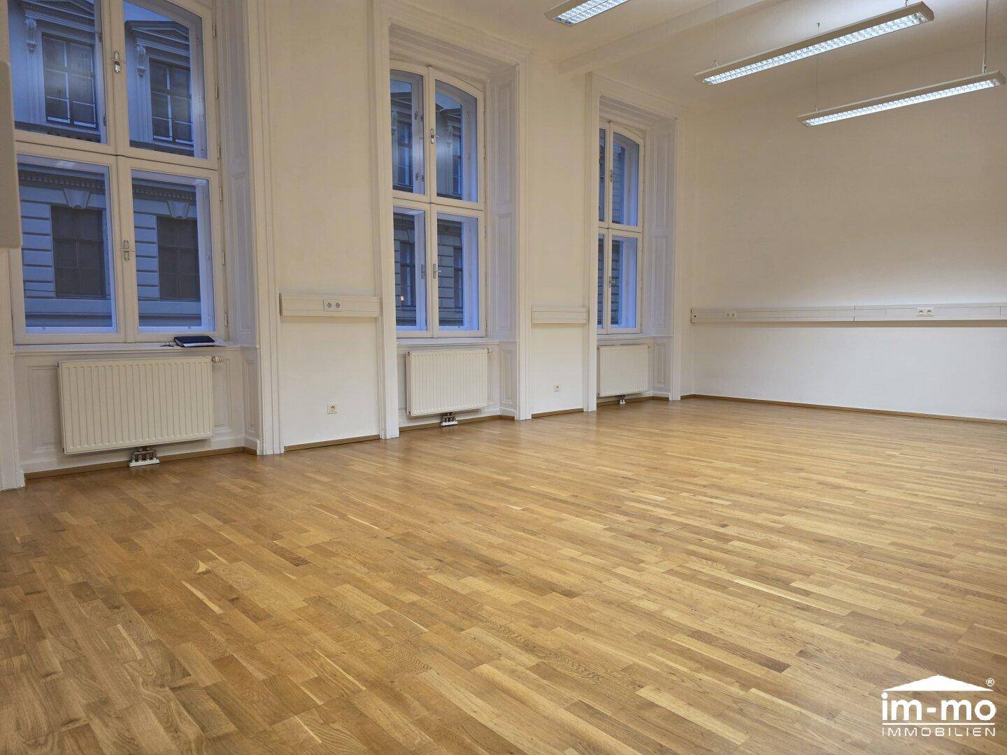 Weitläufiger Raum mit Holzboden und großen Fenstern, bietet viel Tageslicht und Platz.
