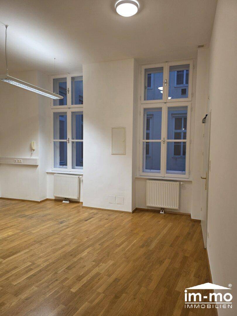 Heller, leerer Raum mit Holzboden und hohen Fenstern, ideal für Büro oder Wohnzwecke.