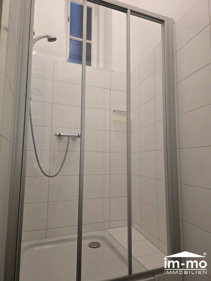 Duschkabine mit weißen Fliesen und einer Glasschiebetür, funktional und sauber.
