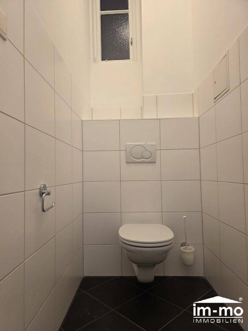Separate Toilette mit Wand-WC und weißen Fliesen, ausgestattet mit dunklem Boden.