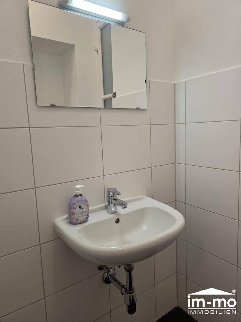 Waschbecken mit Spiegel und Seifenspender in einem einfach gehaltenen Badezimmer.