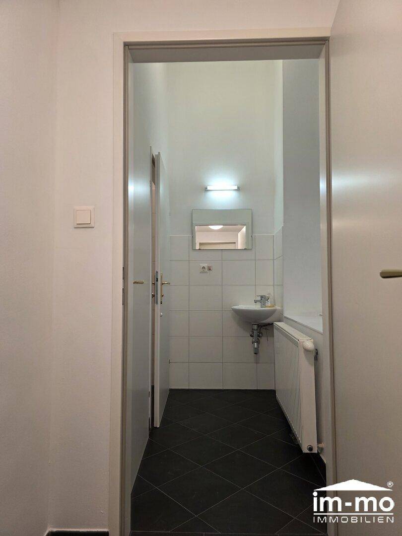 Eingangsbereich zu einem Badezimmer mit Waschbecken und Heizkörper, gefliest.