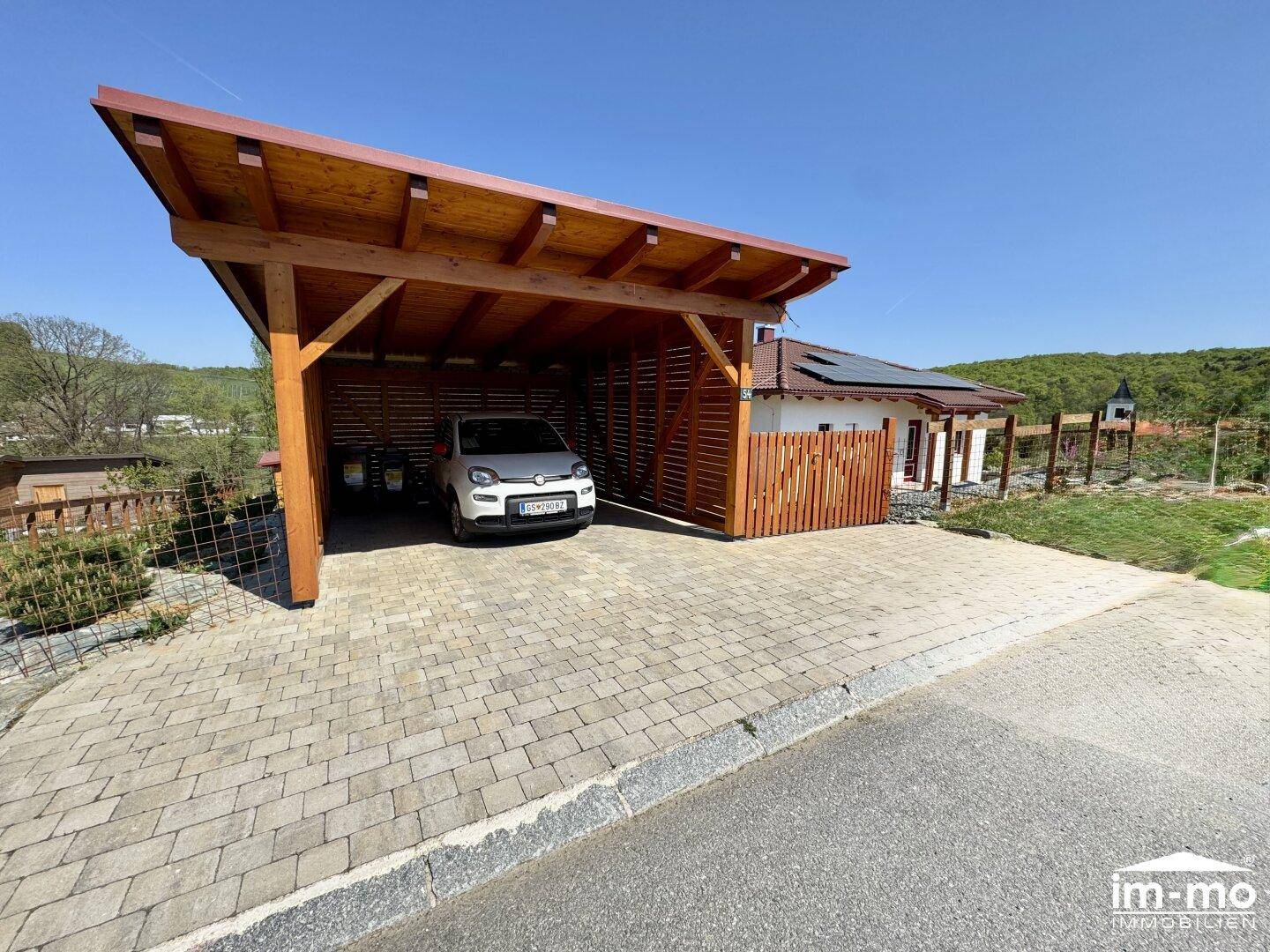 Geräumiger Carport mit Holzelementen und gepflasterter Zufahrt.