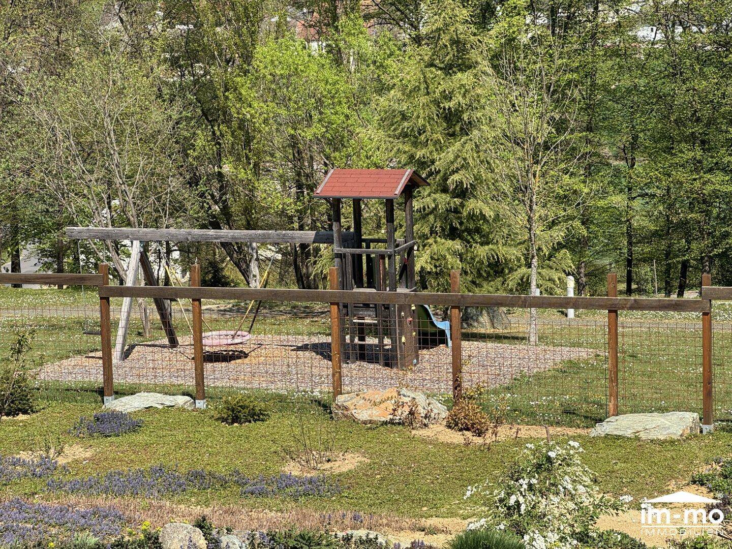 Kinderspielplatz mit Schaukel und Kletterturm in grüner Umgebung.