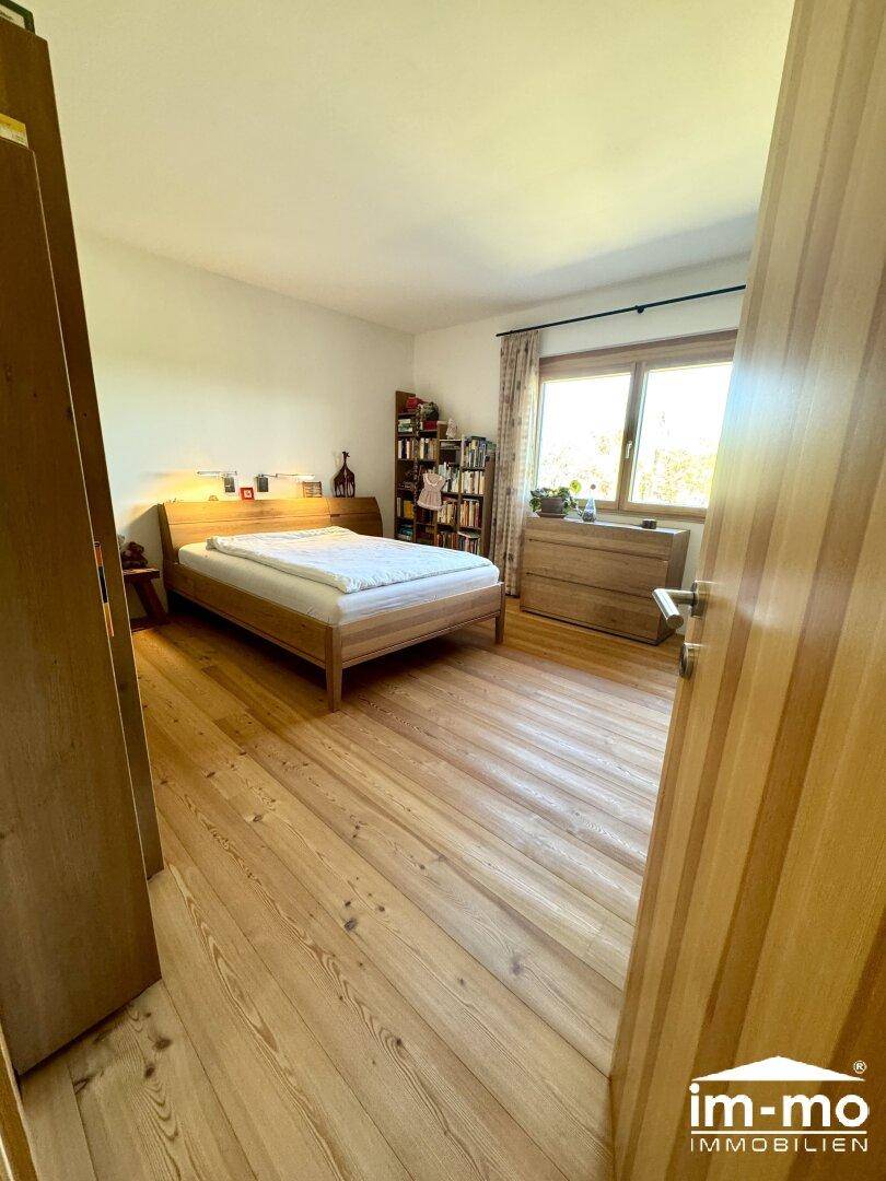 Schlafzimmer mit Holzboden, großem Bett und Fenster mit Blick ins Freie.