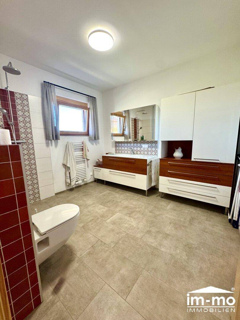 Helles Badezimmer mit großem Waschtisch, Spiegelschrank und Fenster.