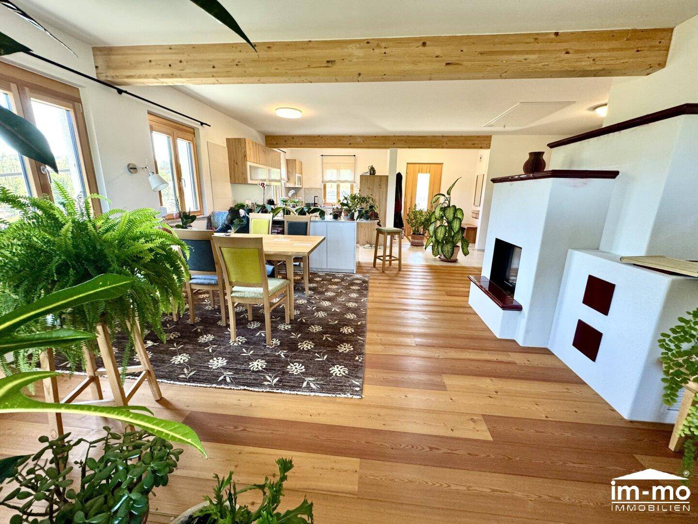 Offener Wohn-Essbereich mit Kamin, Holzbalken und integrierter Küche im Hintergrund.