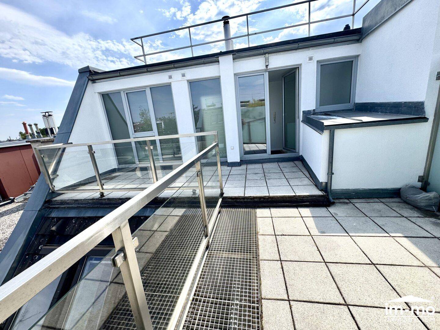 Dachterrasse mit Fliesenboden und Zugang zu den Innenräumen, umgeben von einem Geländer.
