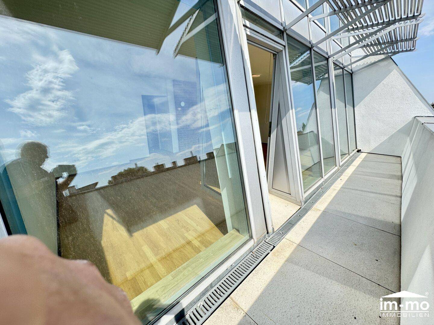 Helle Dachterrasse mit großen Fenstern und Blick auf den Himmel, ideal für sonnige Tage.