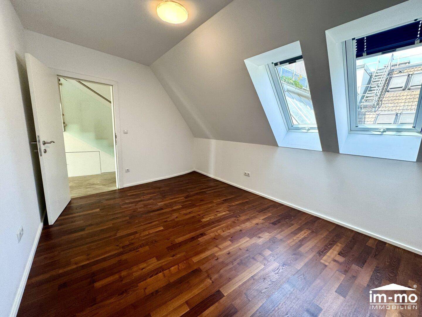 Gemütliches Schlafzimmer mit dunklem Parkettboden und Dachfenstern, bietet viel Tageslicht.
