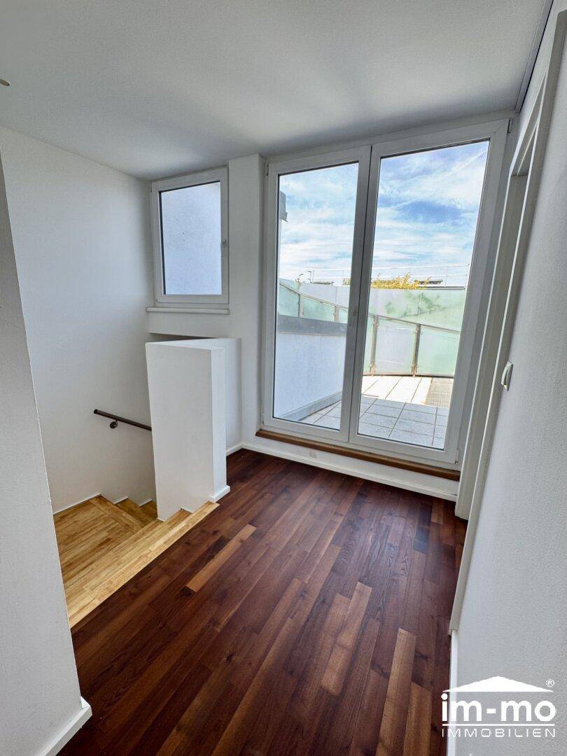 Heller Flur mit dunklem Parkettboden und Zugang zur Terrasse, führt zu einem Treppenaufgang.
