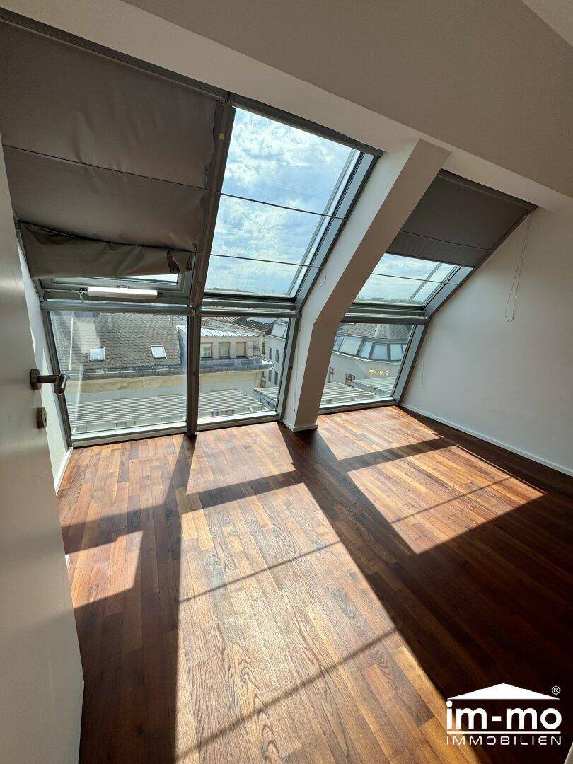 Helles Schlafzimmer mit dunklem Parkettboden und großen Dachfenstern, bietet einen weiten Blick.