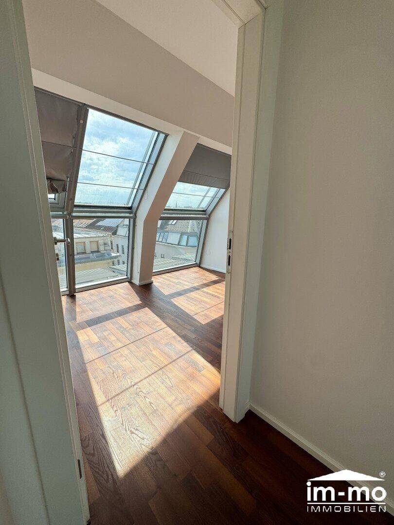 Schlafzimmer mit dunklem Parkettboden und großen Dachfenstern, bietet viel Tageslicht und Ausblick.