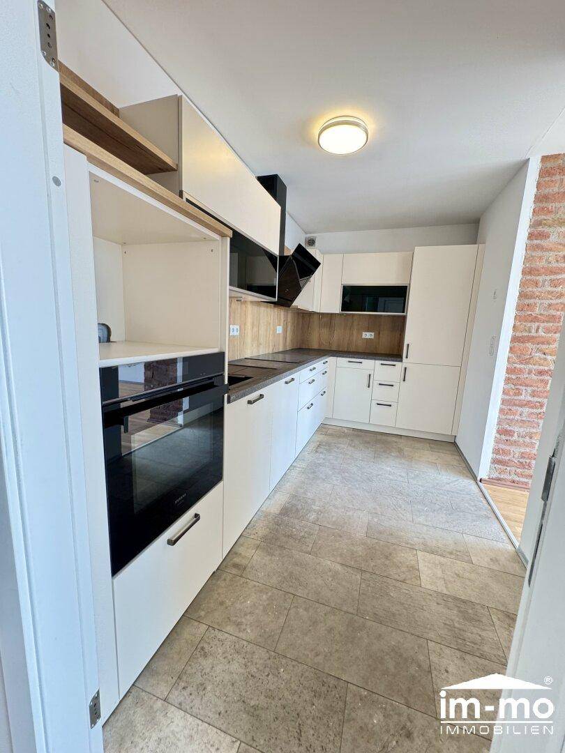 Moderne Küche mit weißen Schränken, integrierten Geräten und Fliesenboden, bereit zum Kochen.