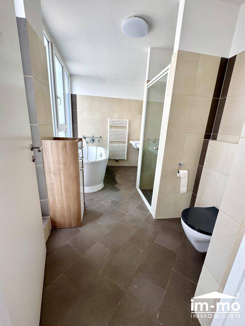 Modernes Badezimmer mit Badewanne, Dusche und WC, hell gefliest und mit Fenster.