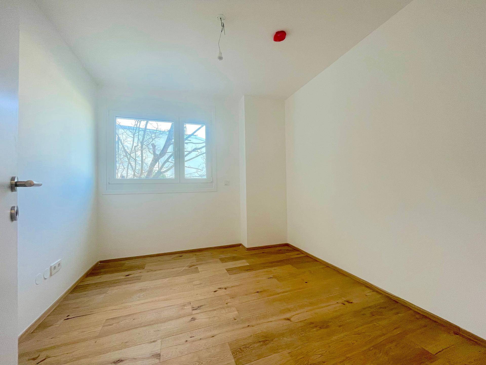 Gemütliches Schlafzimmer mit Holzboden und einem Fenster, das viel Licht spendet.