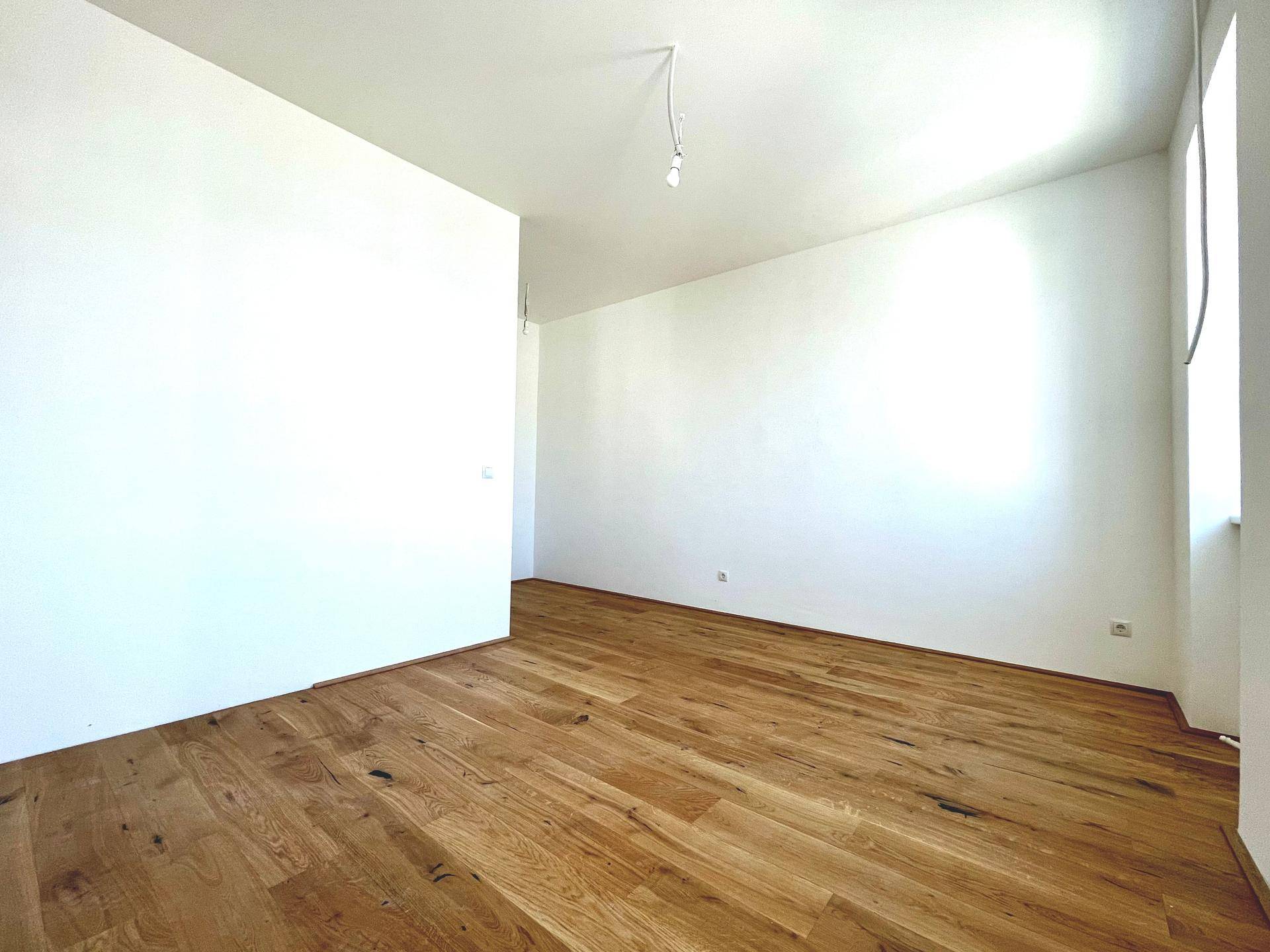 Geräumiger, heller Raum mit neuem Holzparkettboden und einem Fenster, bereit zur Einrichtung.