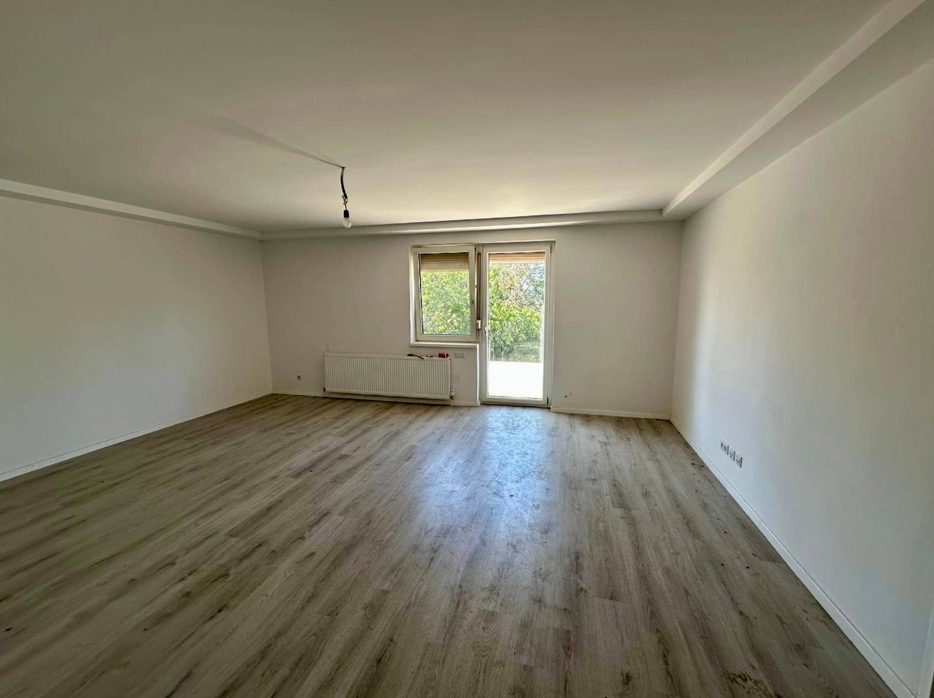 Helles, leeres Zimmer mit neuem Laminatboden und Zugang zur Terrasse, bereit zur Renovierung.