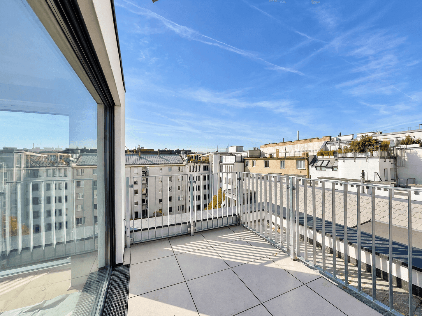 Großer Balkon mit Fliesenboden und Blick auf die umliegenden Gebäude der Stadt.