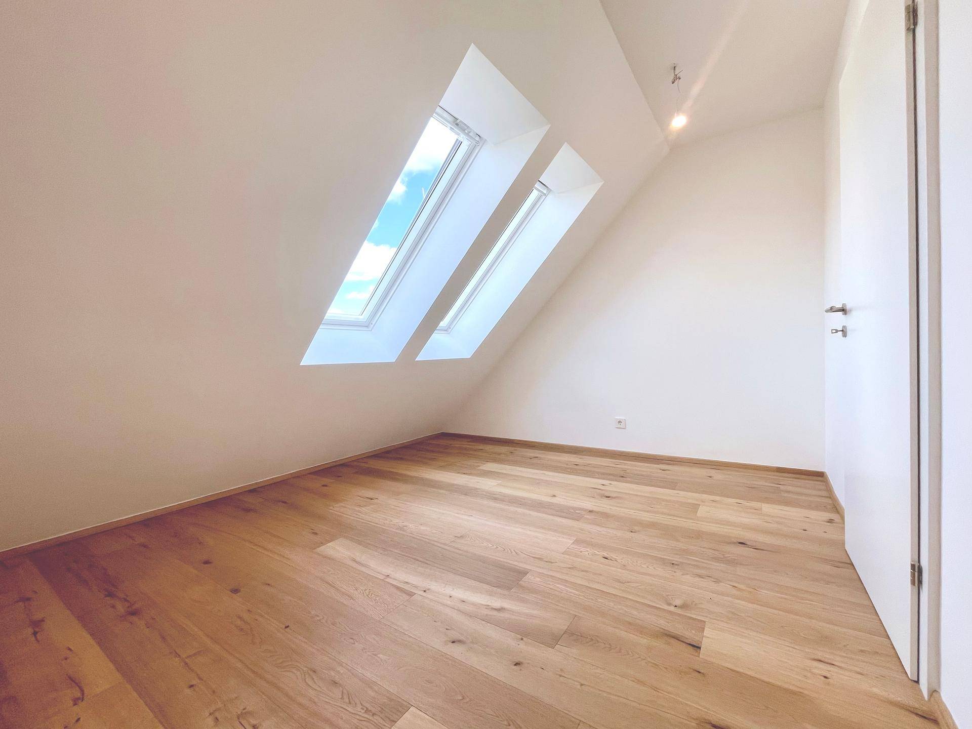 Geräumiges Schlafzimmer im Dachgeschoss mit Holzboden und Dachfenstern, bietet eine helle Wohnatmosphäre.