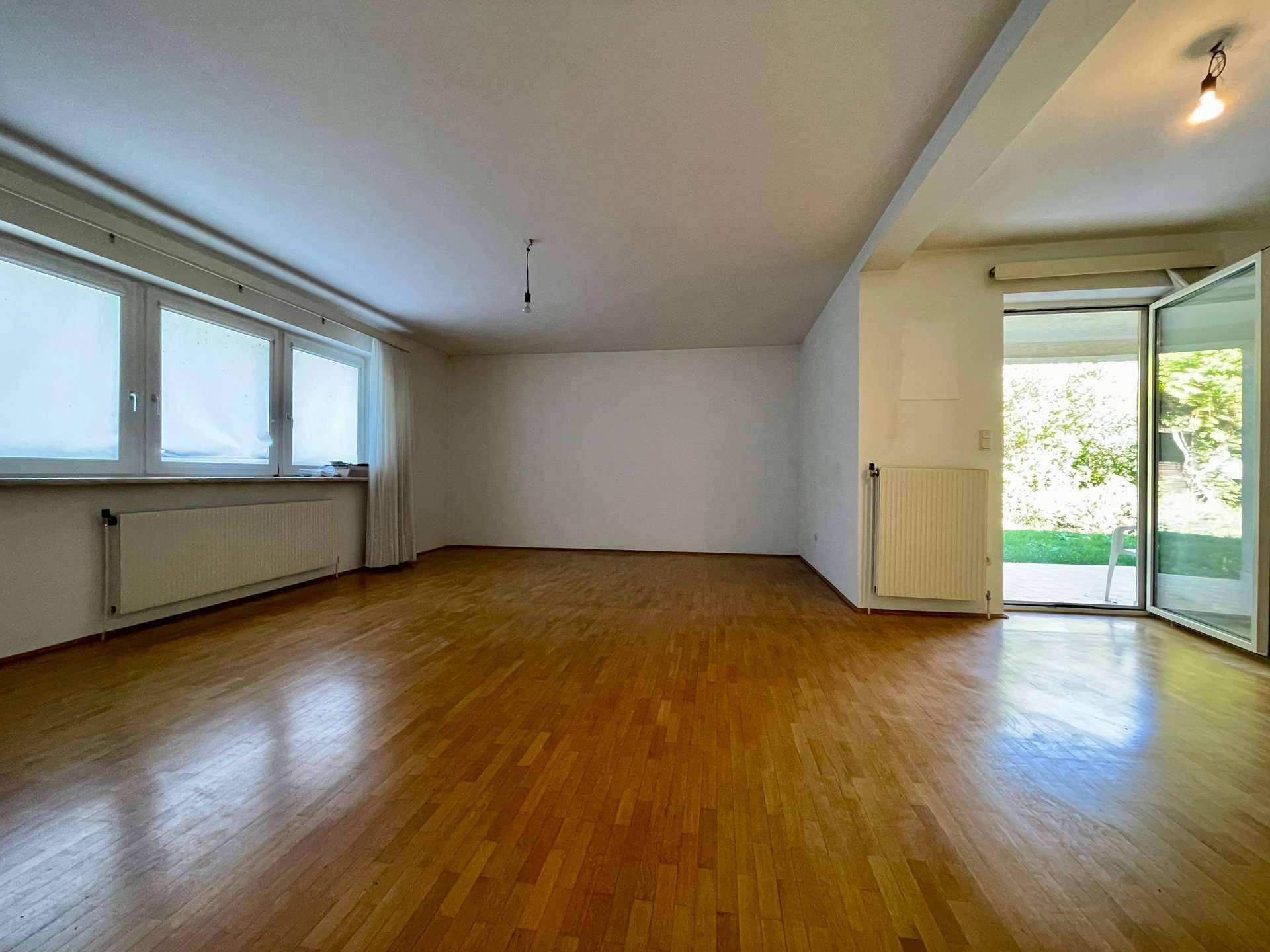 Geräumiges, leeres Wohnzimmer mit Parkettboden und Zugang zum Garten.