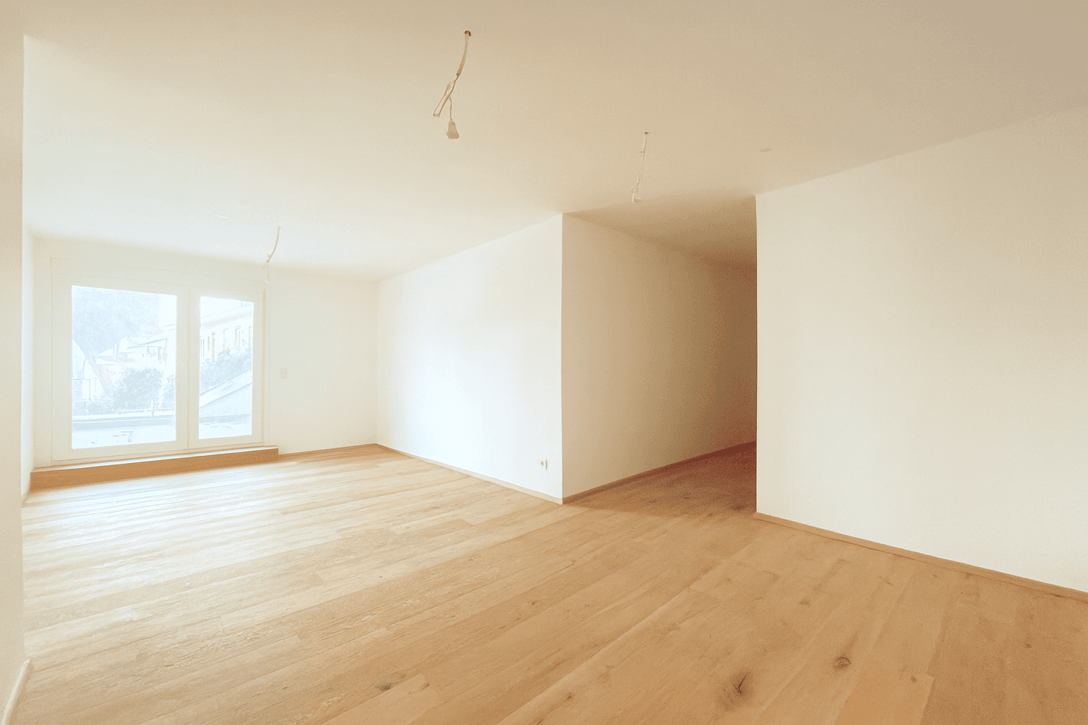 Geräumiger, heller Wohnbereich mit Holzboden und großen Fenstern, bereit zur individuellen Gestaltung.