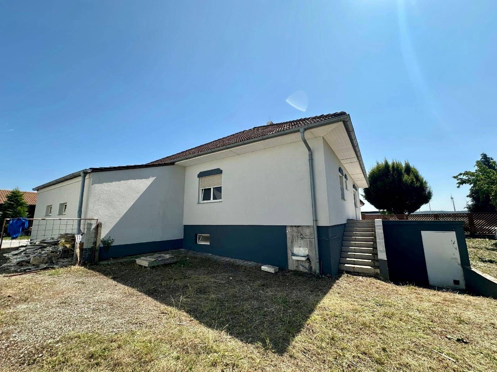 Seitenansicht des Hauses mit Außentreppe und blauem Sockelbereich unter klarem Sommerhimmel.