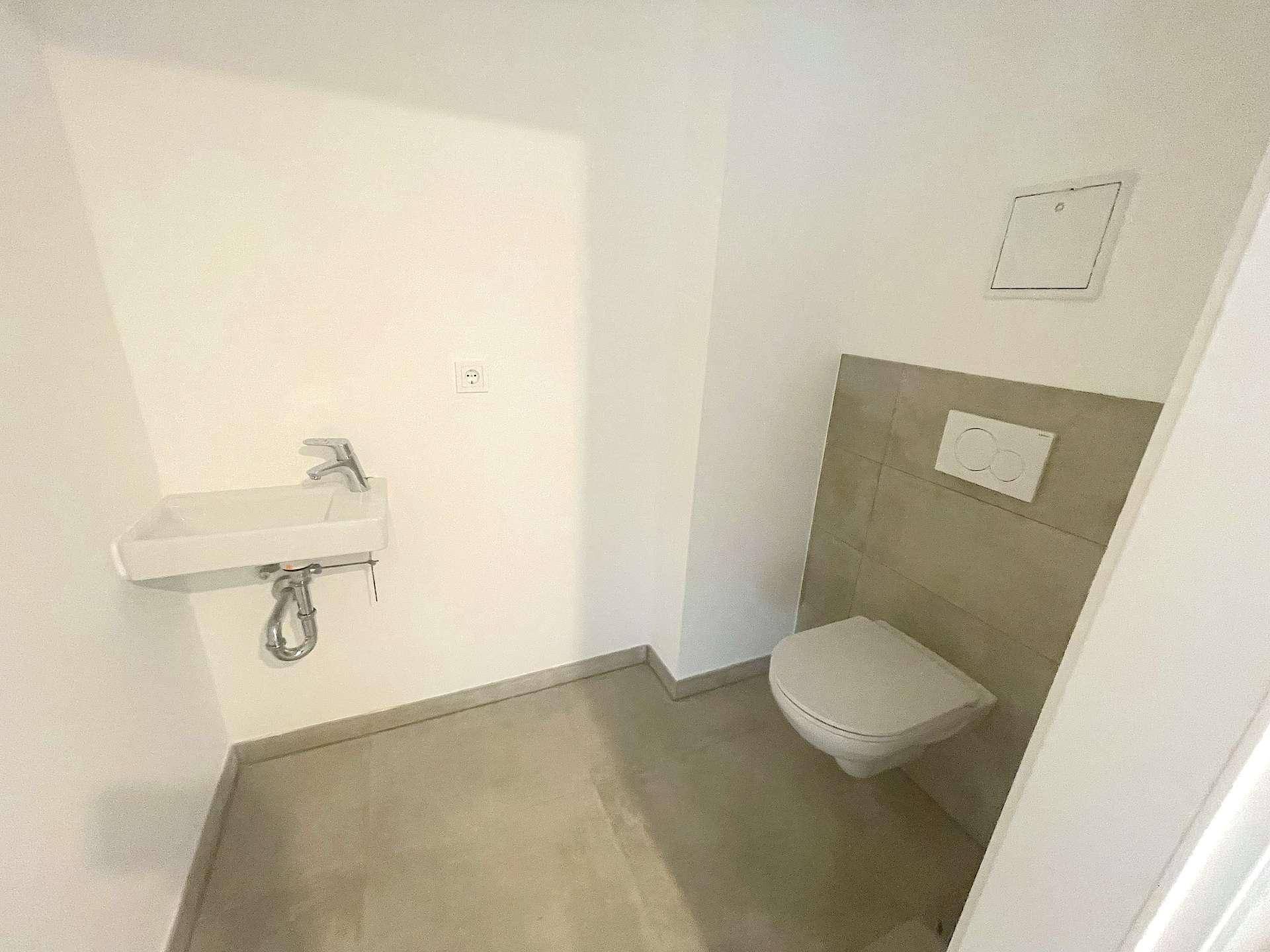 Separates Gäste-WC mit wandhängender Toilette und kleinem Waschbecken, modern gefliest.