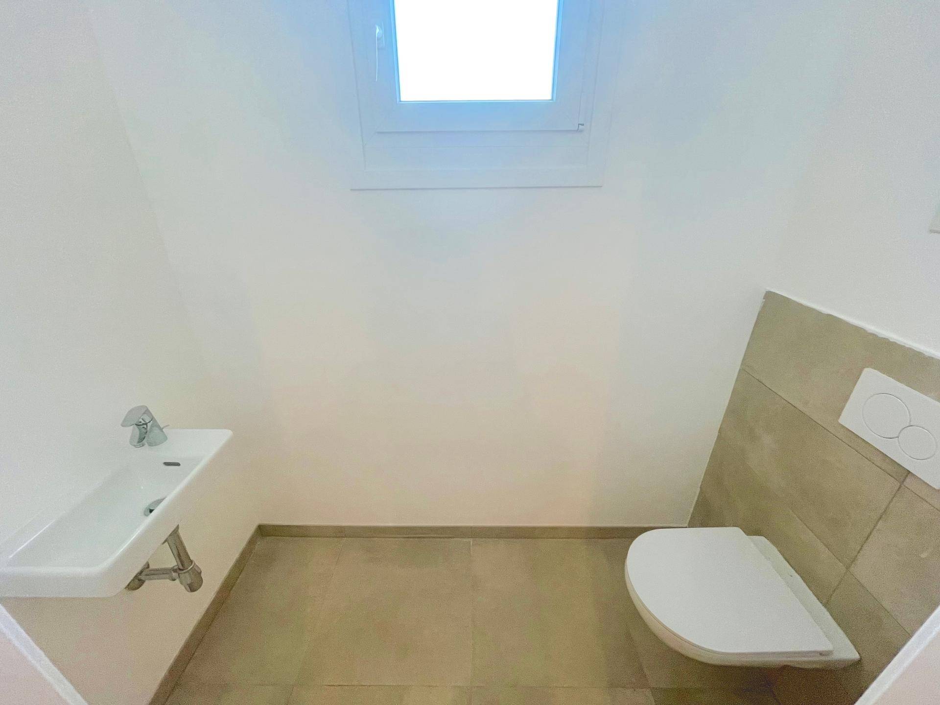 Separates Gäste-WC mit wandhängender Toilette, kleinem Waschbecken und Fenster.
