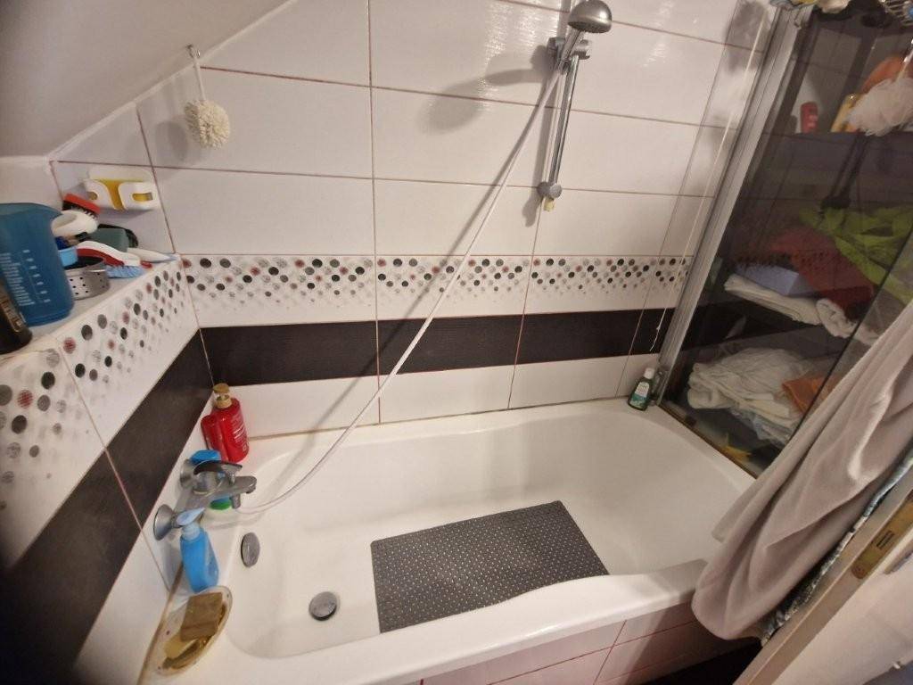 Badewanne mit Duscharmatur und gefliesten Wänden in Schwarz-Weiß-Muster.