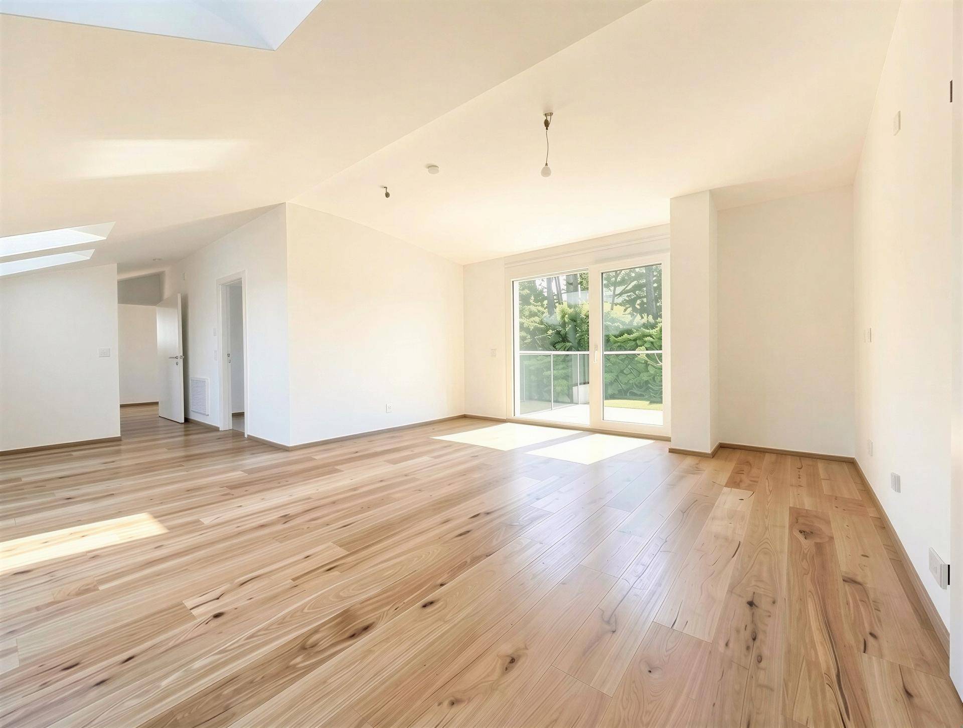 Heller, geräumiger Wohnbereich mit Holzboden, großen Fenstern und Zugang zum Außenbereich, sowie Dachfenstern.
