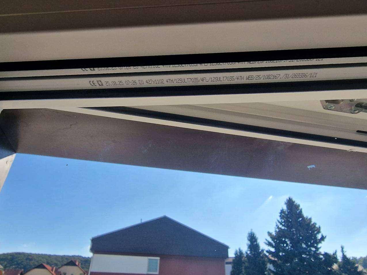 Nahaufnahme eines Fensterrahmens mit sichtbaren technischen Details und Blick auf den Himmel.