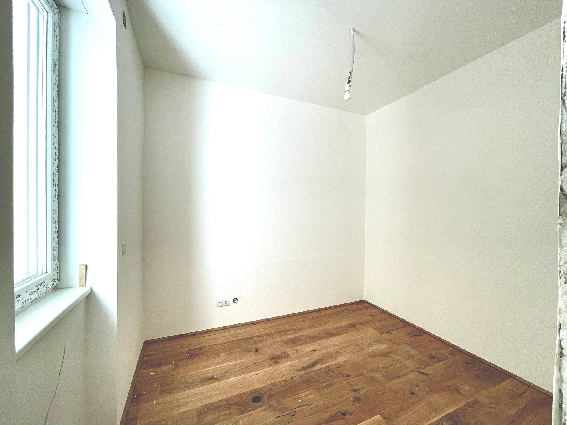 Unmöblierter Raum mit Holzdielenboden und einem Fenster, bereit für den Innenausbau.