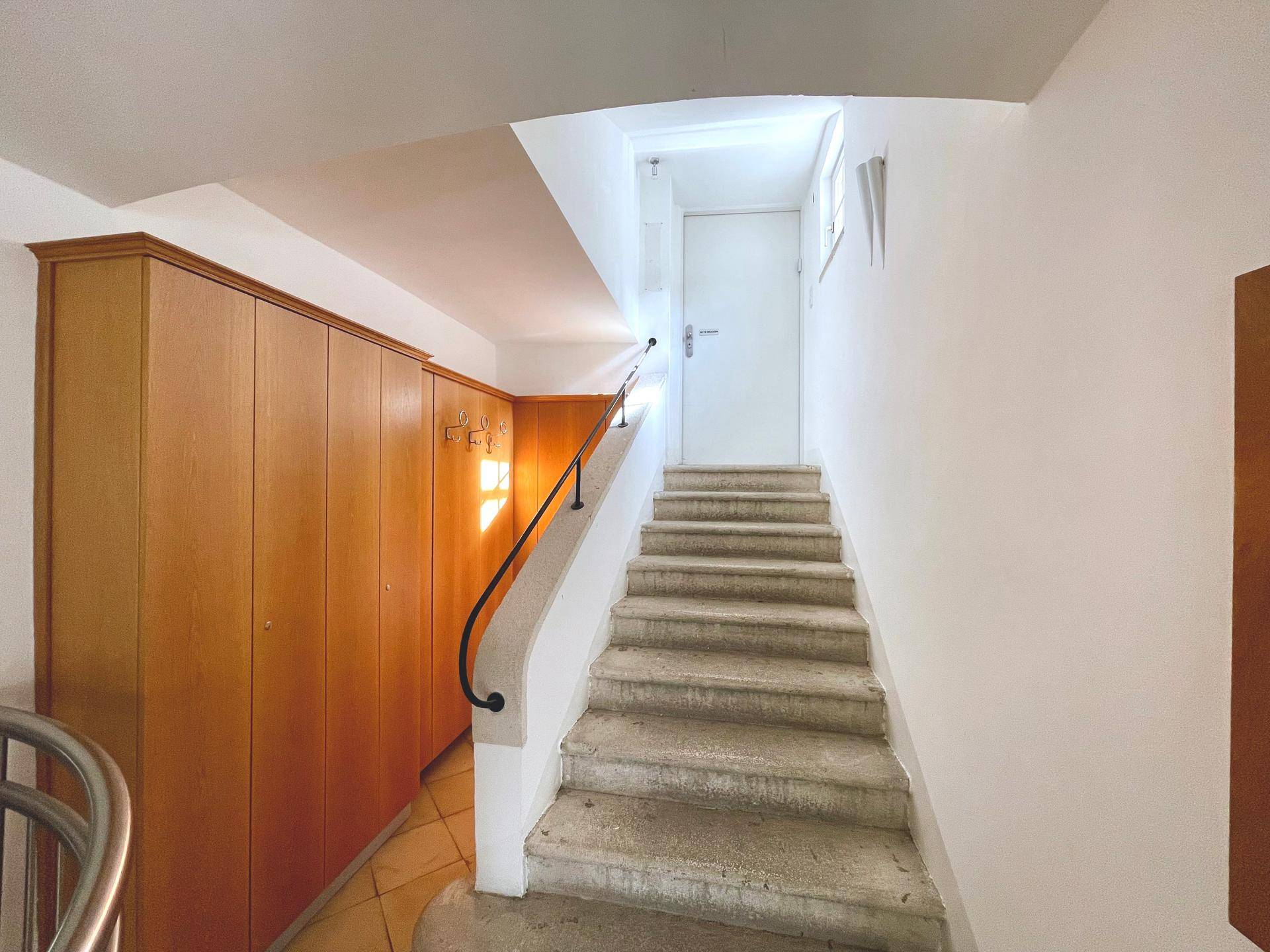Steintreppe mit Holzgeländer und Einbauschränken im Treppenhausbereich, gut erhalten.