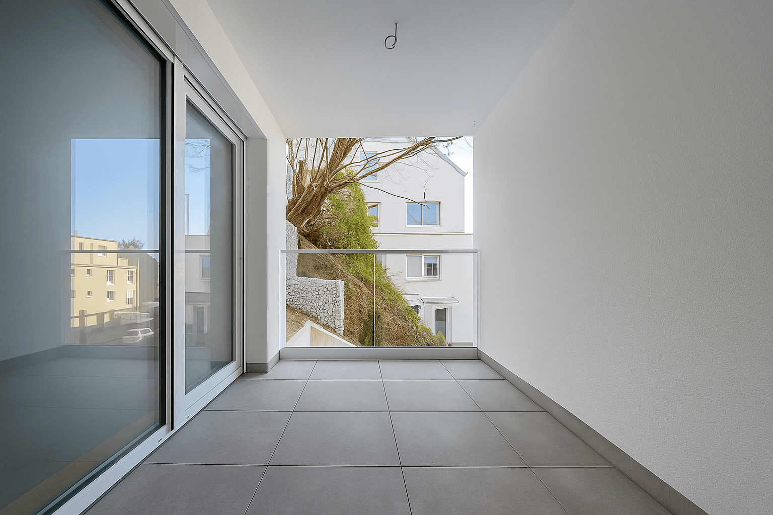 Geräumiger Balkon mit Fliesenboden und Glasgeländer, bietet einen weiten Blick auf die Umgebung.