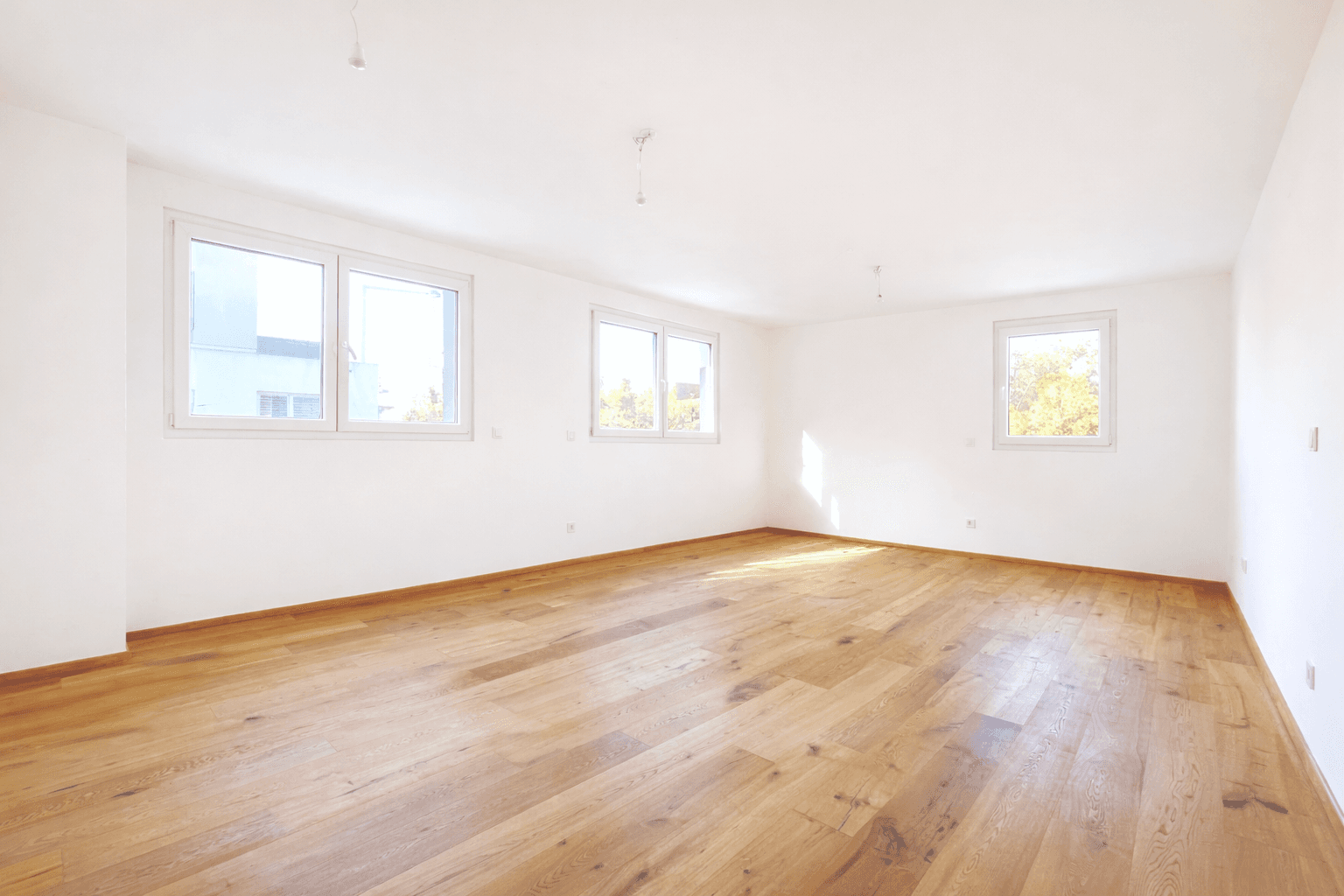 Geräumiges, lichtdurchflutetes Zimmer mit hellem Holzparkett und mehreren Fenstern.
