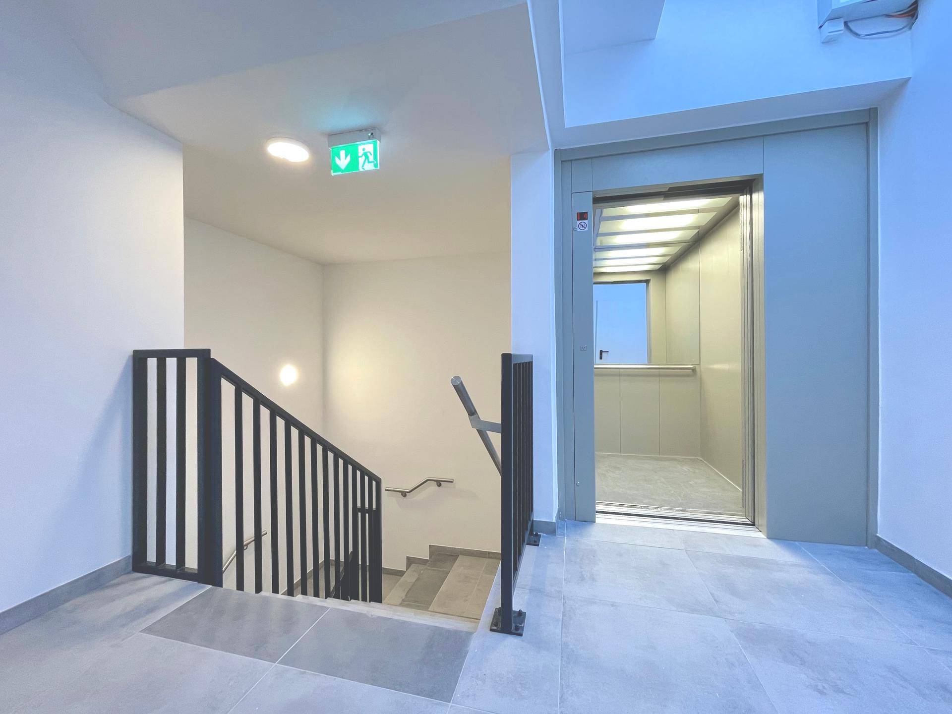 Heller Treppenaufgang mit modernem Geländer und Zugang zum Aufzug, in einem Mehrfamilienhaus.