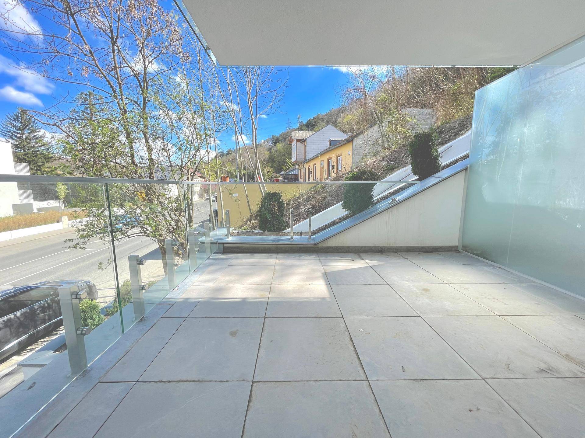 Große, geflieste Terrasse mit Glasgeländer und Blick auf die Umgebung und den Hang.