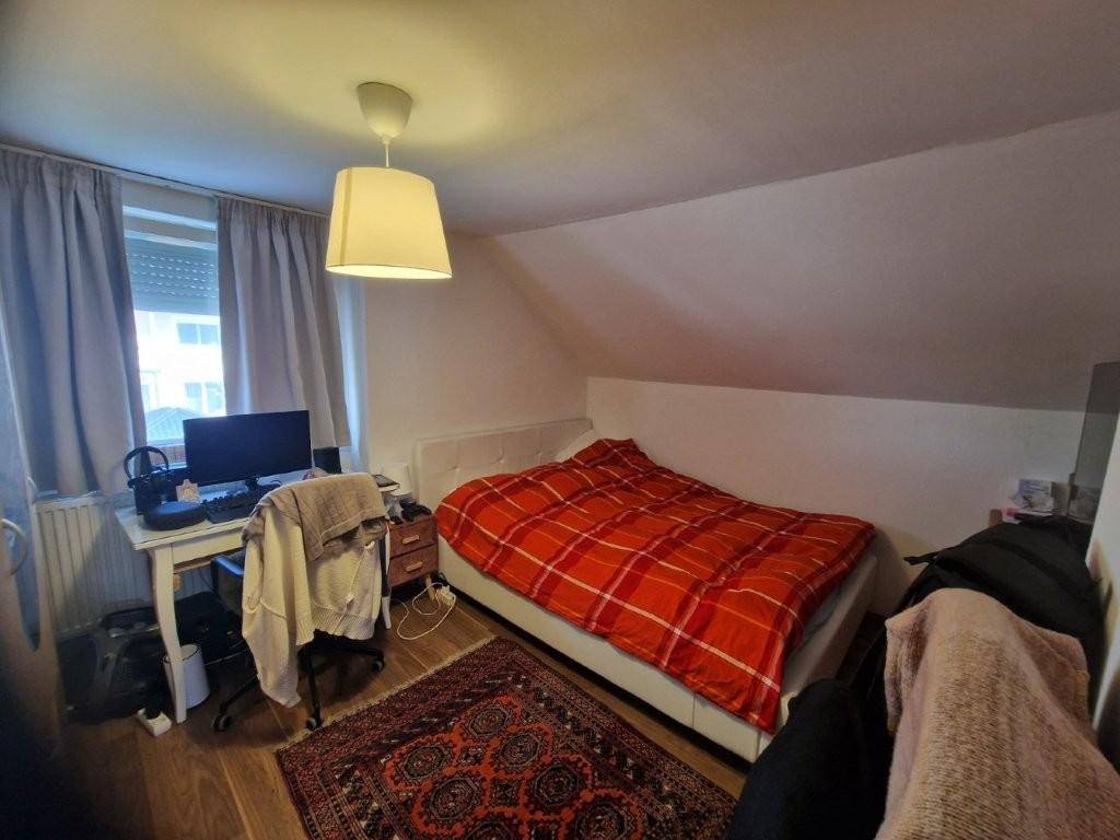 Helles Schlafzimmer mit Einzelbett, Schreibtisch und Dachschräge.