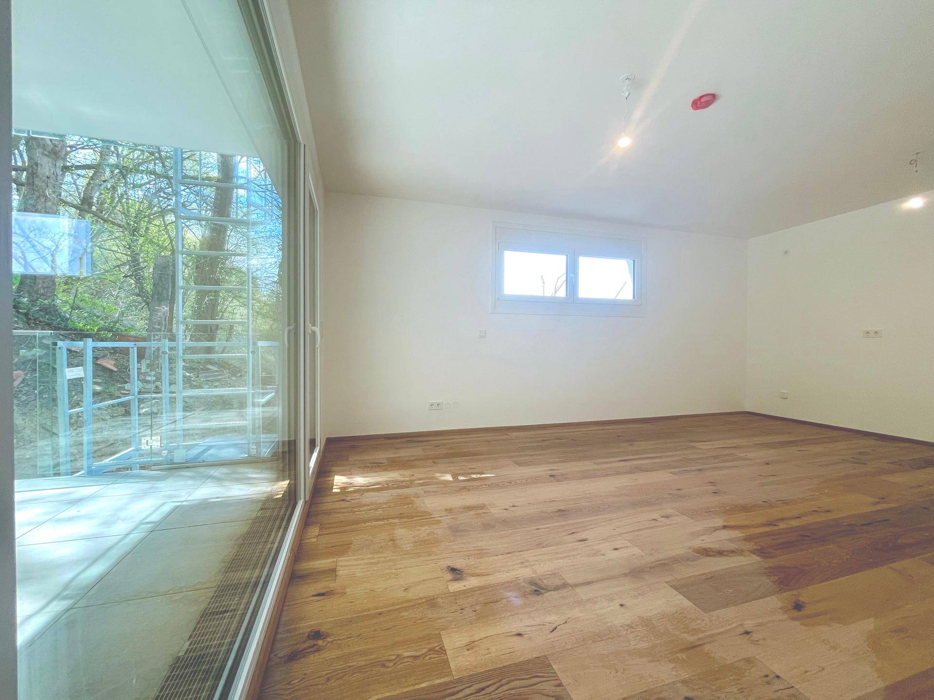 Helles Wohnzimmer mit Holzboden und großen Fenstern, bietet einen grünen Blick auf die Natur.